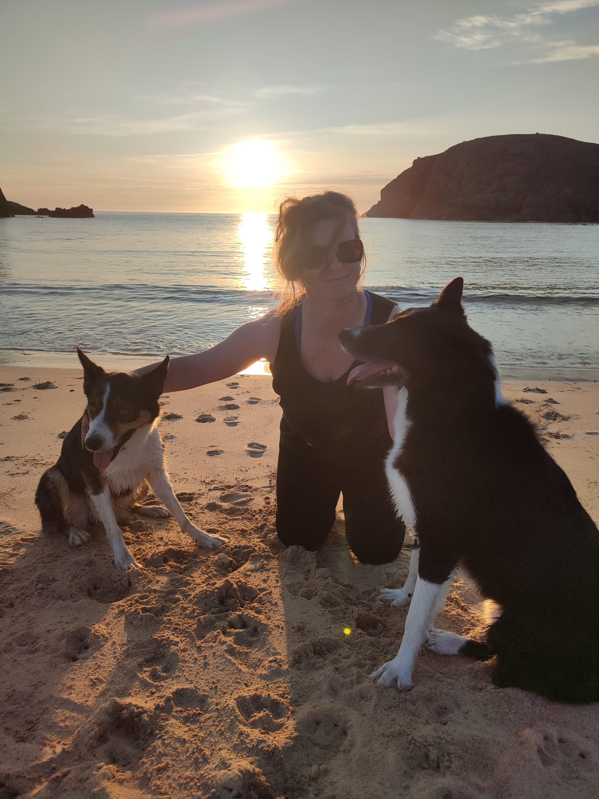 Ann on the beach at sunset with two of her dogs on the Isle of Lewis